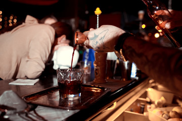 Bartender pouring fresh alcoholic drink into the glasses with ice cubes on the bar counter