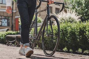 On his way. Close up of young man standing in the park with a bicycle