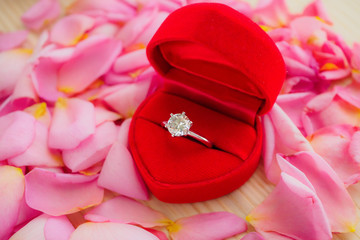 elegant wedding diamond ring in red heart jewelry box on beautiful pink rose petal background close up