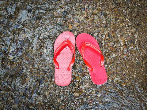 Red flip flops on beach with gravel and water flow wave