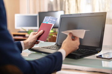 Man holding airline ticket and passport buying on the Internet using a laptop. Purchasing and booking tickets online