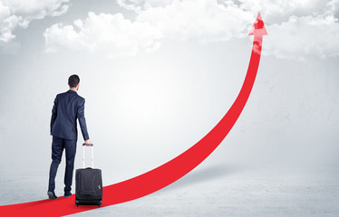 Fototapeta premium Young businessman with back leaving on the red arrow carpet to the skies with luggage on his hand 