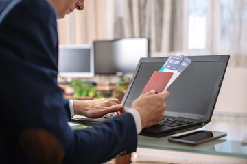 Man holding airline ticket and passport buying on the Internet using a laptop. Purchasing and booking tickets online