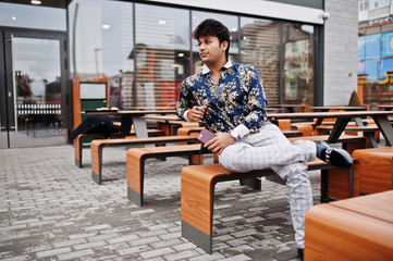 Attractive and handsome stylish indian man wear on shirt, holding mobile phone and sitting in the terrace of modern lounge cafe at his work break.