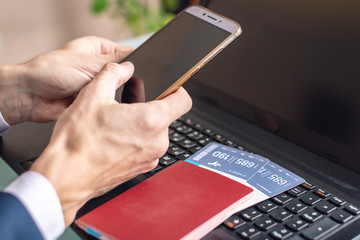 Man holding phone in hand buying on the Internet airline tickets using a laptop. Purchasing and booking online