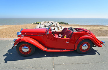 Fototapeta na wymiar Classic Red Singer Motor Car Parked on Seafront Promenade.