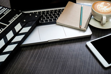 office stuff with Movie clapper, laptop, smartphone, tablet, coffee cup, pen, notepad and documents on the wood table top view shot.