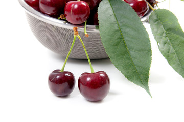 Steel colander with red sweet cherry isolated on a white background..