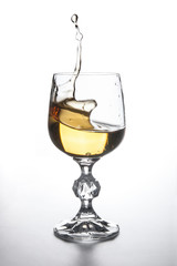 White wine splashing in wine glass on light background. .
