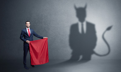 Businessman standing with red cloth in his hand and devil shadow on the background
