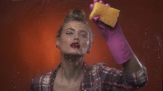 Sexy blonde woman with old school hairstyle is drawing the heart using water on a window