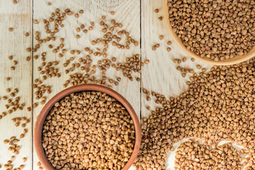 Dry buckwheat in brown clay bowl on wooden table. gluten free grain for healthy diet