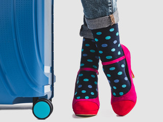 Stylish suitcase, women's legs, bright, multicolored socks and pink shoes on a white, isolated background. Close-up. Concept of style, fashion, beauty and travel