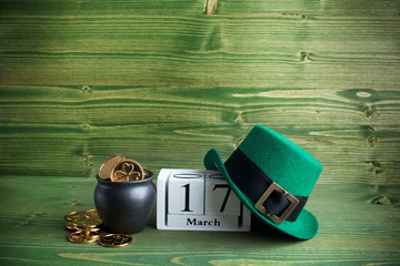 white block calendar for St Patrick's Day, March 17, with Leprechaun hat and pot of gold, on green wooden background.