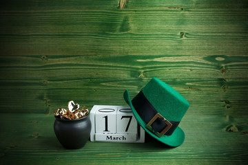 white block calendar for St Patrick's Day, March 17, with Leprechaun hat and pot of gold, on green wooden background.