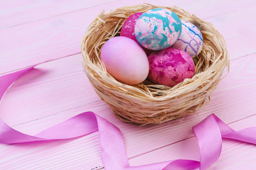 Fototapeta na wymiar Colorful easter eggs in a nest on pink wooden background
