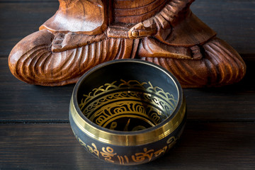 Tibetan singing bowl in front of a sitting wooden buddha