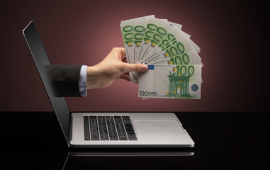 Hand with money coming out of a laptop with sparkling effects
