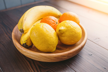 Fresh fruits lemon, orange and banana on a wooden plate and background, as healthy dessert and diet