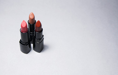 Three lipsticks stand vertically on a white background close to each other in the left side 