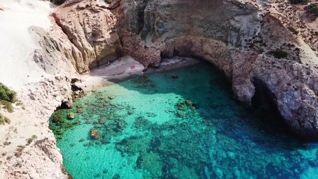 Aerial drone bird's eye view video of iconic volcanic white chalk beach and caves of Tsigrado with turquoise and sapphire clear waters, Milos island, Cyclades, Greece