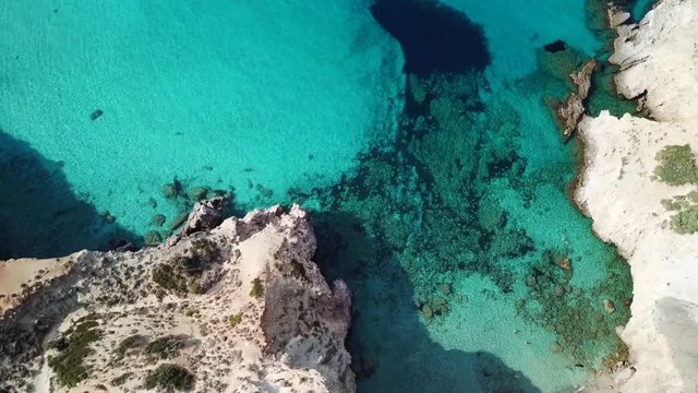 Aerial drone bird's eye view video of iconic volcanic white chalk beach and caves of Tsigrado with turquoise and sapphire clear waters, Milos island, Cyclades, Greece