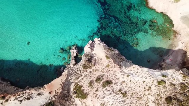 Aerial drone bird's eye view video of iconic volcanic white chalk beach and caves of Tsigrado with turquoise and sapphire clear waters, Milos island, Cyclades, Greece