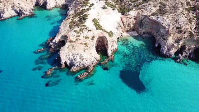 Aerial drone bird's eye view video of iconic volcanic white chalk beach and caves of Tsigrado with turquoise and sapphire clear waters, Milos island, Cyclades, Greece