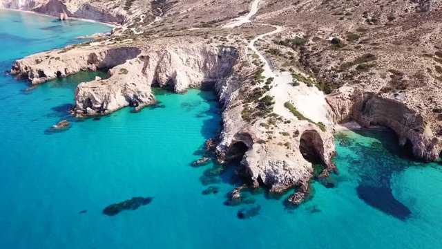 Aerial drone bird's eye view video of iconic volcanic white chalk beach and caves of Tsigrado with turquoise and sapphire clear waters, Milos island, Cyclades, Greece