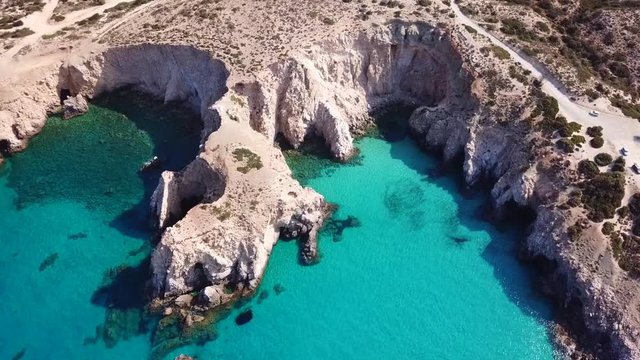 Aerial drone bird's eye view video of iconic volcanic white chalk beach and caves of Tsigrado with turquoise and sapphire clear waters, Milos island, Cyclades, Greece