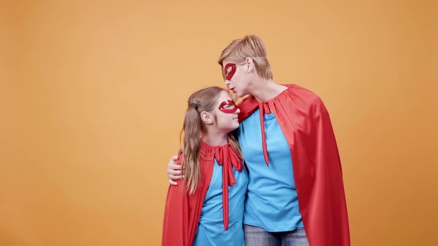 Mom kisses her daughter on the forehead while dressed as superheroes. Encouraging an young dreamer.