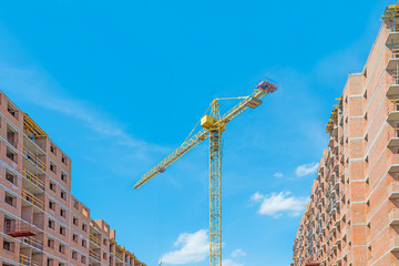 New building concept. A crane on blue sky background with high riser blocks.