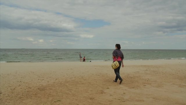 Woman in jeans wear walks along the beach. Shot from back
