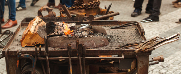 Old blacksmith tools on the medieval fair. Anvil, hammer, fire, chain. Brazier on city the street forge workshop. Forge fire at summer medieval fair.