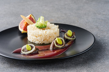 rice, broccoli, fig and fried meat with sauce on black plate and stone surface