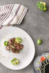 top view of broccoli and fried meat on white plate and fig with onion on black plate