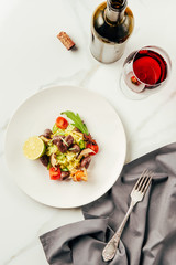 top view of salad on white plate with glass and bottle of wine