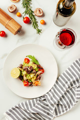 top view of salad on white plate with glass and bottle of wine and cloth