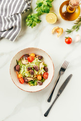 salad on white bowl with bottle of oil, cherry tomatoes, lime and rosemary on table