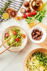 top view of salad on white bowl with bottle of oil, cherry tomatoes, lime and rosemary on surface