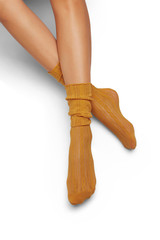 A pair of mustard-colored lace loose socks on lady’s crossed legs, isolated against the solid color background. Glamorous foot-wear with ornament. Voguish legwear for fashionable ladies and girls.