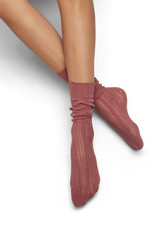 A pair of coral pink lace loose socks on woman’s crossed legs, isolated against the solid color...