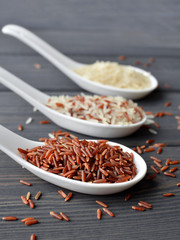 Mixed organic raw rice in spoons over dark desk background