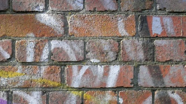 Spray painted brick wall.  Camera tracks across a red brick wall which has been sprayed with graffiti.