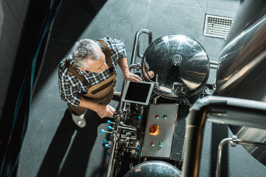 overhead view of male senior brewer using digital tablet in brewery