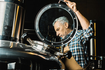 professional male brewer in working overalls checking brewery equipment