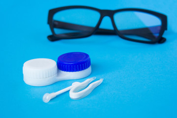 Glasses and container with contact lenses on a blue background. The concept of taking care of vision.