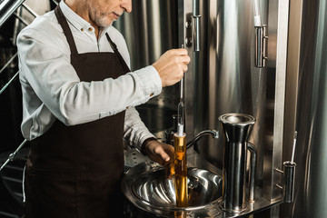 cropped view of senior brewer examining beer in flask in brewery