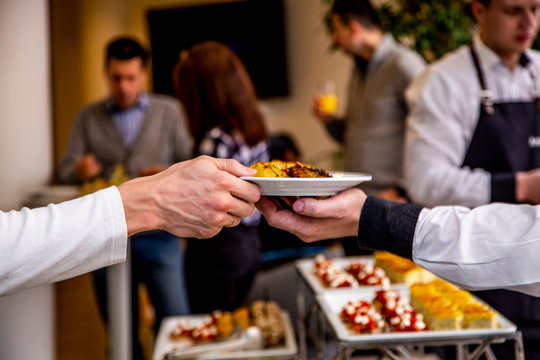 waiter's hand passes a plate of potatoes in the hands of a man at catering event on some festive event, party or wedding reception