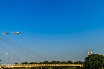 Suspension bridge spanning across Nan river to Phichit railway station in Muang district of Phichit province with blue sky and sunshine. Phichit is a province of Thailand and far 330 km from Bangkok.